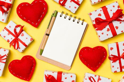 Holiday composition of notebook, gift boxes and red textile hearts on colorful background with empty space for your design. Top view of Valentine's Day concept photo