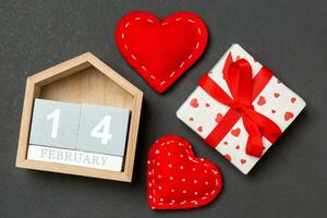 Composition of wooden calendar, holiday white gift boxes and red textile hearts on colorful background. The fourteenth of February. Valentine's day concept photo