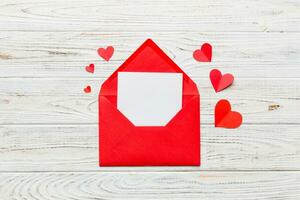 Red paper envelope with empty white card and heart on colored background. top view valentines day concept photo