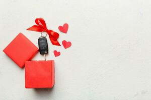 Black car key in a present box with a ribbon and red heart on colored background. Valentine day composition Top view photo