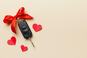 Car key with a red bow and a heart on Colored table. Giving present or gift for valentine day or christmas, Top view with copy space photo