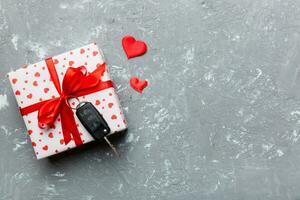 Black car key in a present box with a ribbon and red heart on colored background. Valentine day composition Top view photo