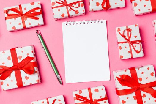 Holiday composition of notebook and gift boxes with red hearts on colorful background with empty space for your design. Top view of Valentine's Day concept photo