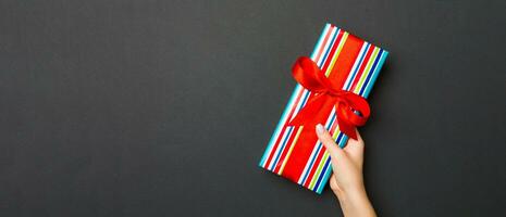 Top view of female hands holding christmas or other holiday handmade present box package in the palms, flat lay on black background with copy space photo