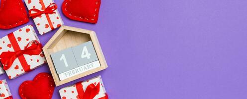 Top view of gift boxes, wooden calendar and red textile hearts on colorful background. The fourteenth of february. St Valentine's day concept with copy space photo