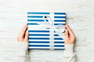 Flat lay of woman hands holding gift wrapped and decorated with bow on white rustic wooden background with copy space. Christmas and holiday concept photo