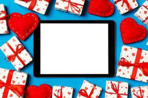 Top view of digital tablet surrounded with gift boxes and hearts on colorful background. Saint Valentine's day photo