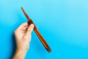 Crop image of male hand holding chopsticks on blue background. Japanese food concept with copy space photo