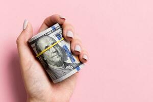 Female hand holding tightly a rolled bundle of money. Top view of one hundred dollars on colorful background. Investment concept with copy space photo