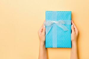 Flat lay of woman hands holding gift wrapped and decorated with bow on gold background with copy space. Christmas and holiday concept photo