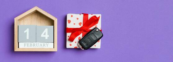 Top view of car key on a gift box with red hearts and festive calendar on colorful background. The fourteenth of february. Present for Valentine's Day concept photo