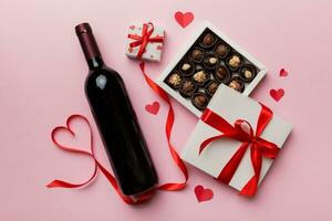 Bottle of red wine on colored background for Valentine Day with gift and chocolate. Heart shaped with gift box of chocolates top view with copy space photo