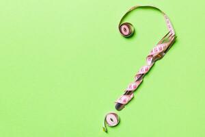 Top view of question mark made of fork and measuring tape on green background. Diet concept with copy space photo