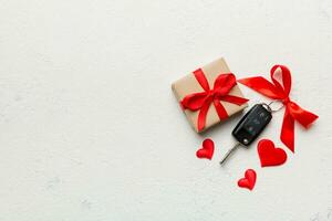 Black car key in a present box with a ribbon and red heart on colored background. Valentine day composition Top view photo