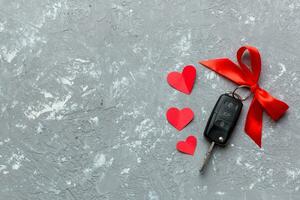 Car key with a red bow and a heart on Colored table. Giving present or gift for valentine day or christmas, Top view with copy space photo