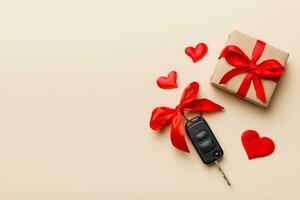 Black car key in a present box with a ribbon and red heart on colored background. Valentine day composition Top view photo