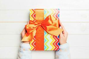 woman hands holding gift wrapped and decorated with colored bow top view on white wooden table Holiday concept with copy space photo