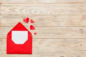 Red paper envelope with empty white card and heart on colored background. top view valentines day concept photo