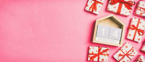 Holiday composition of gift boxes with red hearts and wooden calendar on colorful background with empty space for your design. The fourteenth of February. Top view of Valentine's Day concept photo