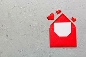 Red paper envelope with empty white card and heart on colored background. top view valentines day concept photo