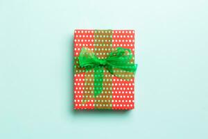 wrapped Christmas or other holiday handmade present in paper with green ribbon on blue background. Present box, decoration of gift on colored table, top view with copy space photo