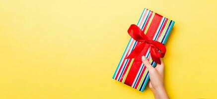 Woman arms holding gift box with colored ribbon on yellow table background, top view and copy space for you design photo