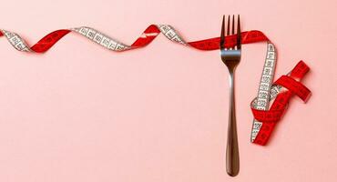 Fork surrounded with curled tape measure on pink background with copy space. Top view of proper diet concept photo
