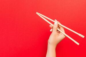 Woman's hand holding chopsticks on red background. Chinese food concept with empty space for your design photo