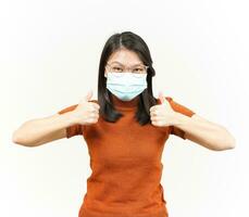 Wearing Medical Mask for Preventing Corona Virus And Showing Thumbs Up Of Beautiful Asian Woman Isolated On White Background photo