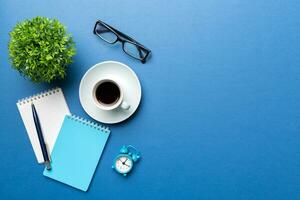 Modern office desk table with notebook and other supplies with cup of coffee. Blank notebook page for you design. Top view, flat lay photo