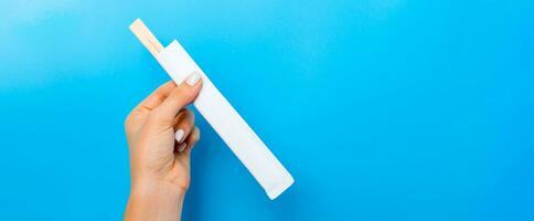 Female hand holding a packet with chopsticks on blue background. Sushi concept with empty space for your idea photo