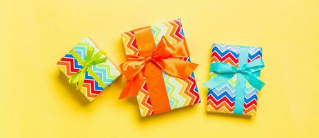 Gift box with blue, green and orange bow for Christmas or New Year day on yellow background, top view photo