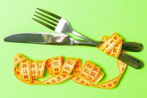 Diet concept with fork, knife and measuring tape on green background. Top view of weight loss photo