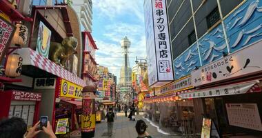 Tourists taking pictures of Osaka famous Tsutenkaku tower. Typical street Japan video