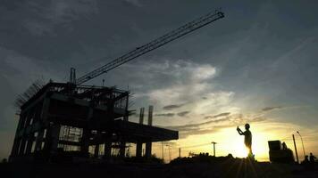 silhueta do engenheiro e escavadora trabalhando em construção site, construção local às pôr do sol dentro tarde tempo. video