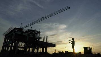 silhueta do engenheiro e escavadora trabalhando em construção site, construção local às pôr do sol dentro tarde tempo. video