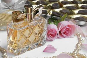 Perfume bottle with rose, rose petals, pearls and chocolates on a light background. photo