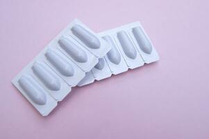 Gynecological medicines for women's health in form of suppository, capsules on pink background. photo