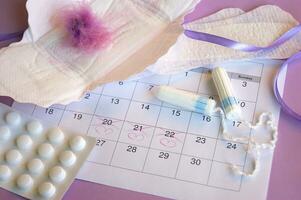 Menstrual pads and tampons on menstruation period calendar with on lilac background. photo