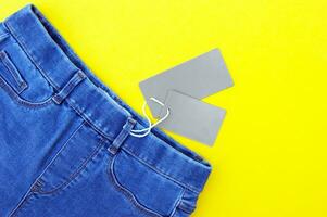 Flat lay, detail of jeans, blank grey labels on yellow background. photo