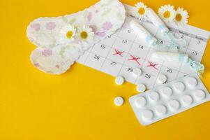 Menstrual pads and tampons on menstruation period calendar with chamomiles on yellow background. photo