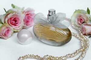 Perfume bottle with rose and pearls on a light background. photo