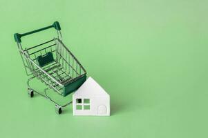 Mini shopping trolley with a white house on a green background. photo