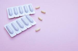 Gynecological medicines for women's health in form of suppository, capsules on pink background. photo