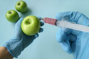 Green apple and syringe with GMO in hands on a blue background. photo