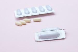 Gynecological medicines for women's health in form of suppository, capsules on pink background. photo