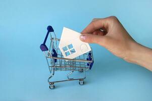 A hand puts a paper white house in a mini shopping trolley. photo