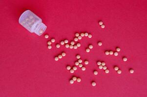 Inverted jar with orange pills on a pink background photo