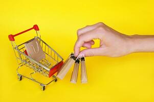 Mini cart and female hand with small craft bags on yellow background. photo