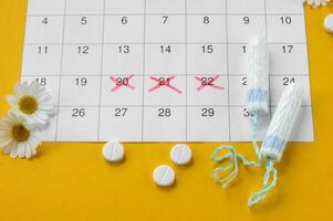 Menstrual tampons on menstruation period calendar with chamomiles on yellow background. photo